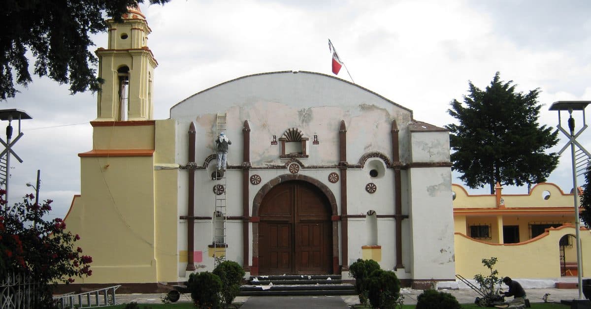 Fachada blanca de la iglesia de San Pedro y San Pablo en San Mateo Atenco, con su torre amarilla y un jardín al frente
