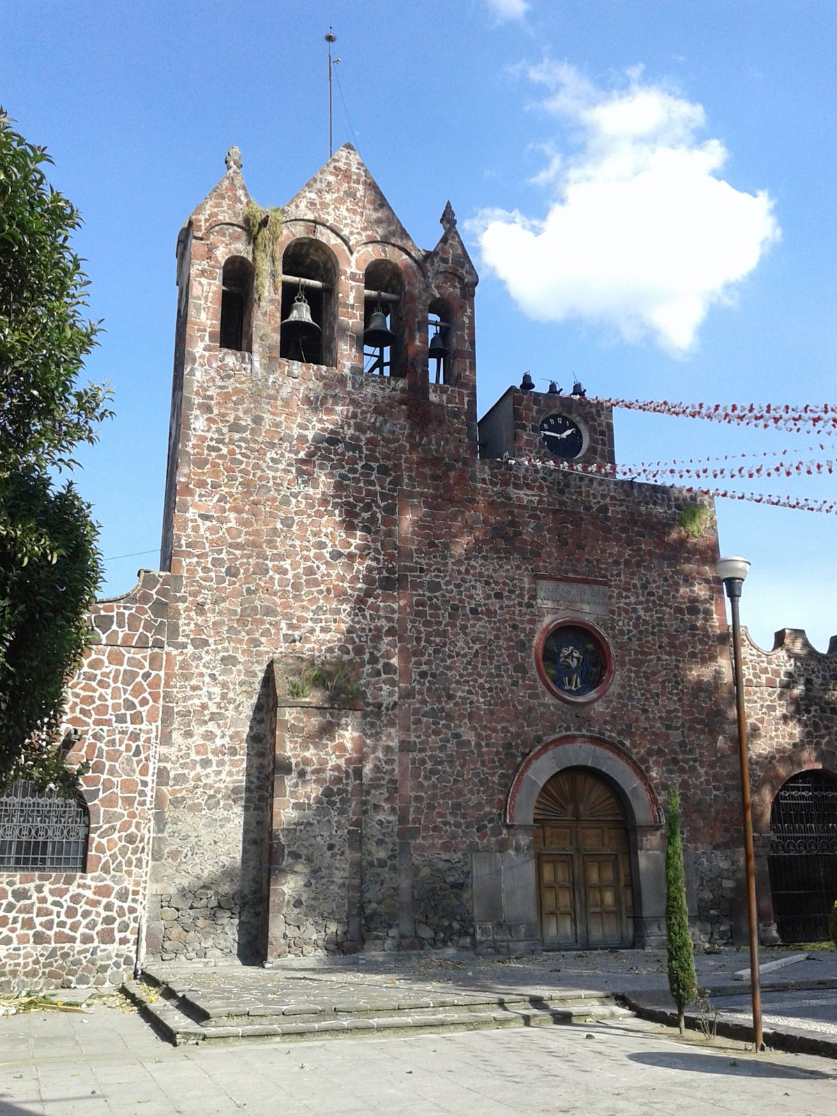Parroquia de San Mateo Apóstol, de piedra rojiza, con su campanario de tres arcos y un reloj en la fachada
