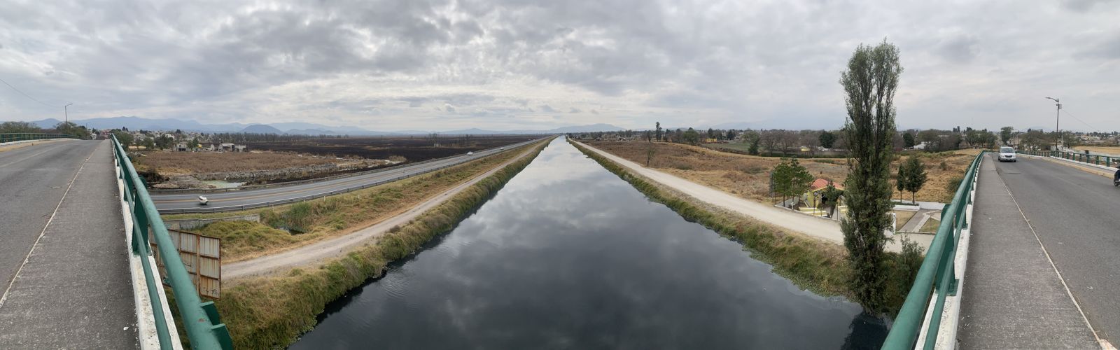 El río Lerma visto desde un puente, encauzado entre bordos de pasto seco y campos de cultivo